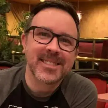 Raymond (bearded, glasses) smiling in a close-up selfie at a restaurant booth, Long Beach dog walker