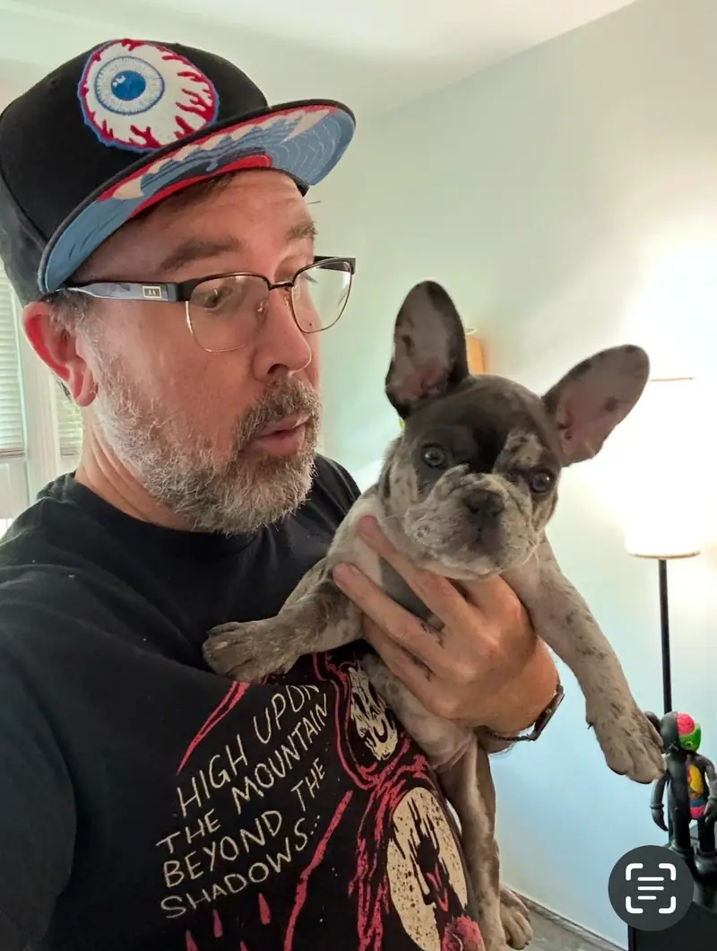 Raymond in a cap and glasses holding a fawn French bulldog indoors, Long Beach dog walker