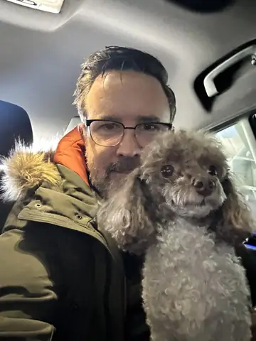 Raymond in a dark jacket in a car, cheek-to-cheek with a gray poodle, Long Beach dog walker
