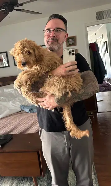 Raymond holding an apricot doodle in his arms in a living room, Long Beach dog walker